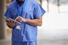 An anonymous doctor in hospital scrubs checks a tablet