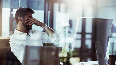 A tired man puts his hands over his eyes while sat at his desk