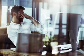 A tired man puts his hands over his eyes while sat at his desk