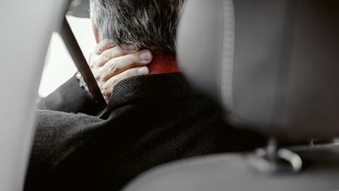 A man in a car holds his neck in pain