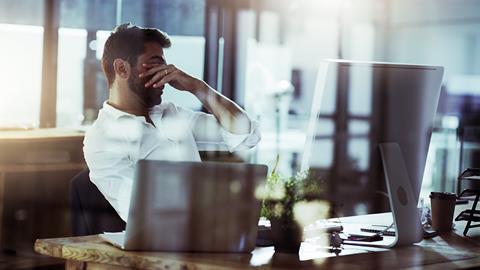 A tired man puts his hands over his eyes while sat at his desk
